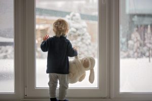 child-with-stuffed-toy-looking-out-the-window-at-the-snow